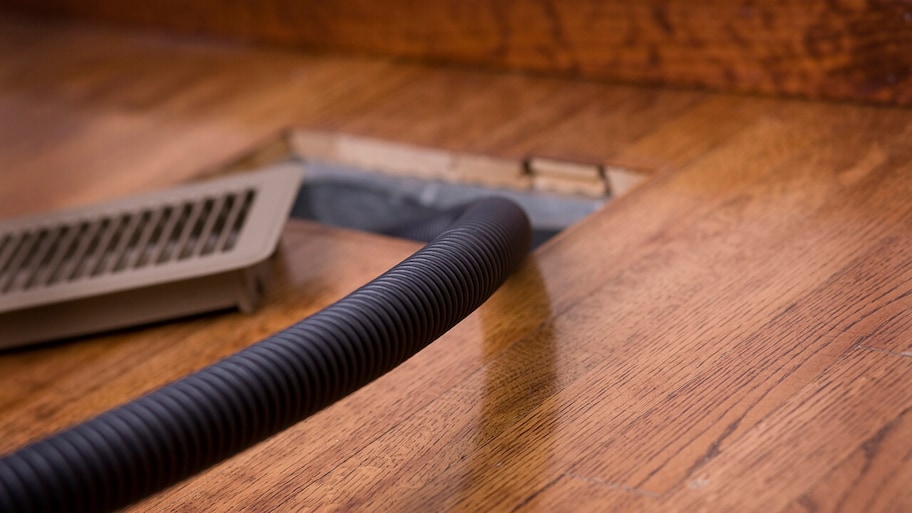 vacuum hose cleaning vent in wooden floor of home